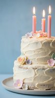 Elegant white frosted birthday cake decorated with pink roses and purple flowers, topped with three lit pink candles on blue background for celebration.