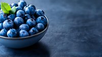 Fresh ripe blueberries in ceramic bowl with mint leaf on dark blue background, selective focus. Food photography for healthy eating concept.