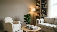 Modern minimalist living room interior with beige sofa, white armchair, wooden bookshelf, and natural lighting creating cozy atmosphere for home decor.