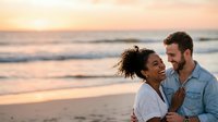 Young multiethnic couple enjoying romantic moment on beach at sunset, man with dark beard wearing denim shirt and woman with curly hair in white top, golden hour coastal scene for relationship and lifestyle content.