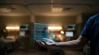 Healthcare professional holds a glowing holographic patient monitor display in a hospital ward, showcasing futuristic medical technology.