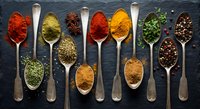 Colorful spices and herbs arranged in vintage wooden spoons on dark slate background for culinary cooking and seasoning recipes.