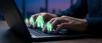 Real estate agent typing on laptop with glowing green house icons floating above keyboard representing digital property search and online home buying.