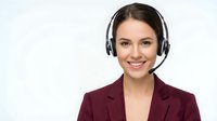 Smiling young Caucasian businesswoman wearing headset and burgundy blazer isolated on white background for customer service and telemarketing concepts.