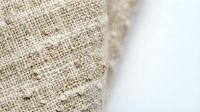 Close-up of natural linen burlap fabric texture with frayed edges on white background, showing organic woven pattern for textile design.