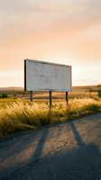 Empty weathered billboard stands beside rural road at golden hour sunset with warm light casting long shadows on asphalt and tall grass swaying in countryside landscape.