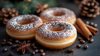 Fresh donuts dusted with powdered sugar on dark background with coffee beans, cinnamon sticks, star anise and pine cones, festive winter food styling.