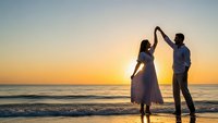 Romantic couple dancing on beach at sunset with golden sky and ocean waves, silhouetted against warm evening light for wedding and love concepts.