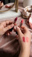 Woman hands holding luxury lipsticks with color swatches on marble vanity table with mirror and silk scarf for beauty makeup routine and cosmetics testing.