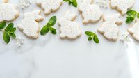 White iced Christmas cookies with mint leaves arranged on marble surface, festive holiday baking and seasonal dessert preparation for winter celebrations.