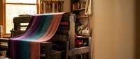 Colorful striped textile draped over vintage wooden furniture in rustic workshop interior with natural lighting and traditional crafting tools.