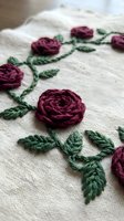 Hand embroidered burgundy roses with green leaves on natural linen fabric showcasing traditional needlework and decorative stitching techniques for crafting projects.