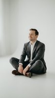 Confident businessman in gray suit sitting cross-legged on floor with genuine smile, representing success and relaxed leadership in modern workplace.