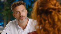 Caucasian man with salt and pepper beard wearing white v-neck t-shirt listens attentively during conversation, showing genuine interest and engagement.