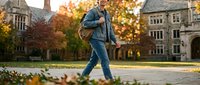 Student walking across campus courtyard with backpack during autumn season, surrounded by fall foliage and historic stone buildings.