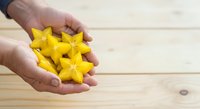 Young adult hand holding fresh yellow star fruit on wooden surface for culinary and healthy eating content.