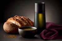 Rustic artisan bread loaf with olive oil bottle and spices in ceramic bowl on dark background with burgundy textile, moody food photography composition.