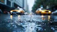 Raindrops splashing on city street with yellow taxis in blurred background creating dramatic urban atmosphere during rainfall. Macro water crown formation.