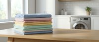 Stack of colorful folded towels on wooden table in modern laundry room with washing machine. Clean fresh linens ready for storage after wash cycle.