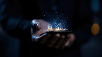Glowing digital business charts and graphs floating above smartphone held in male hands against dark background, representing financial technology growth.