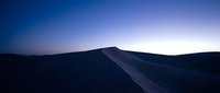 Silhouetted sand dune ridge against twilight sky with gradient purple and blue tones, suitable for travel and nature backgrounds.