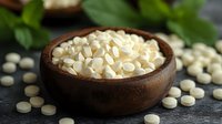 White round pills or tablets in wooden bowl on dark stone background with green leaves, pharmaceutical and medical concept for healthcare industry.