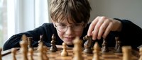 Young boy with glasses concentrating on chess game, strategic thinking and intellectual development through board games for educational content.