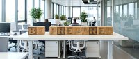 Young professional woman with light skin tone working at desk in modern office space with be prepared wooden blocks, plants, and natural light for business motivation and workplace themes.