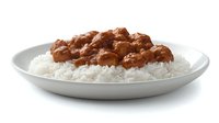 Tender meat chunks in rich brown gravy sauce served over fluffy white steamed rice on round ceramic plate, appetizing comfort food meal presentation.