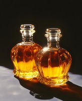 Two elegant crystal decanters filled with golden amber liquid creating warm reflections on white surface against dark background for luxury dining.