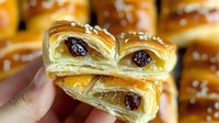 Flaky layered pastry with raisins and honey glaze held in hands showing delicate puff texture and golden brown crust, close up view of fresh baked sweet dessert.
