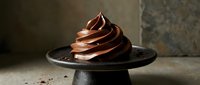 Elegant chocolate frosting swirl on dark plate against textured stone background for bakery and dessert photography projects.