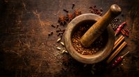 Wooden mortar and pestle with aromatic spices including star anise, cinnamon, chili peppers and seeds on rustic dark wood background for cooking and seasoning.