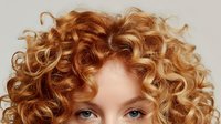 Closeup of natural red curly hair with defined ringlets against neutral background, showcasing voluminous texture and healthy shine for haircare advertising.