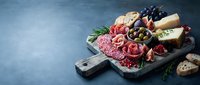 Gourmet charcuterie board with assorted meats, cheeses, olives and herbs on rustic wooden cutting board for entertaining and appetizer presentations.