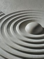 Smooth stone in zen garden with concentric circles in white sand, creating peaceful ripple effect for meditation and mindfulness practices.
