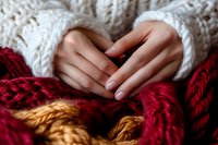 Female hands with natural manicure in cozy white knitted sweater sleeves holding soft burgundy and orange yarn balls, close up winter mood composition.