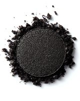 Crushed black eyeshadow powder with scattered particles on white background, macro shot showing fine texture and shimmer detail for cosmetic and beauty content.