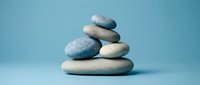 Balanced stack of smooth river stones in zen arrangement on soft blue background for meditation and wellness concepts.