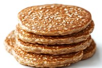 Stack of homemade whole grain pancakes with sesame seeds on top, photographed with selective focus showing detailed texture and golden-brown color.