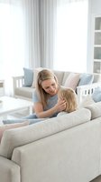 Loving blonde mother embracing young child on modern sofa in bright living room with soft natural lighting creating warm family bonding moment at home.