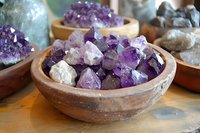 Raw amethyst crystals displayed in rustic clay bowls on wooden surface, featuring purple and white mineral formations with natural geometric patterns.