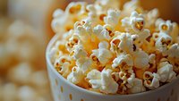 Fresh popcorn in white bowl with shallow depth of field, golden kernels visible. Perfect for food blogs, movie night promotions, or snack advertisements.