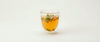 Glass of golden herbal tea with fresh mint leaves on white background, suitable for beverage, wellness, and culinary design projects.