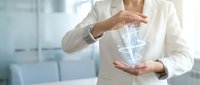 Professional businesswoman in white suit protecting digital lightbulb hologram with hands representing innovation protection and intellectual property security.