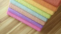 Stack of folded colorful bath towels in pastel rainbow colors arranged on wooden surface, fresh clean cotton terry cloth textiles for bathroom and spa.