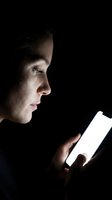 Young woman with light skin tone, brown hair, and focused expression reading from glowing smartphone screen against black background. Suitable for technology, communication, and digital content themes.