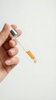 Hand holding glass dropper bottle with golden serum oil drop for skincare beauty routine cosmetic treatment on neutral background.