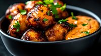 Crispy golden meatballs with herbs served in creamy orange sauce in dark bowl, comfort food ready for dinner menu and restaurant presentation.