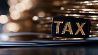 Golden tax text on black label against blurred stacked coins background, representing financial and taxation concepts for business accounting.